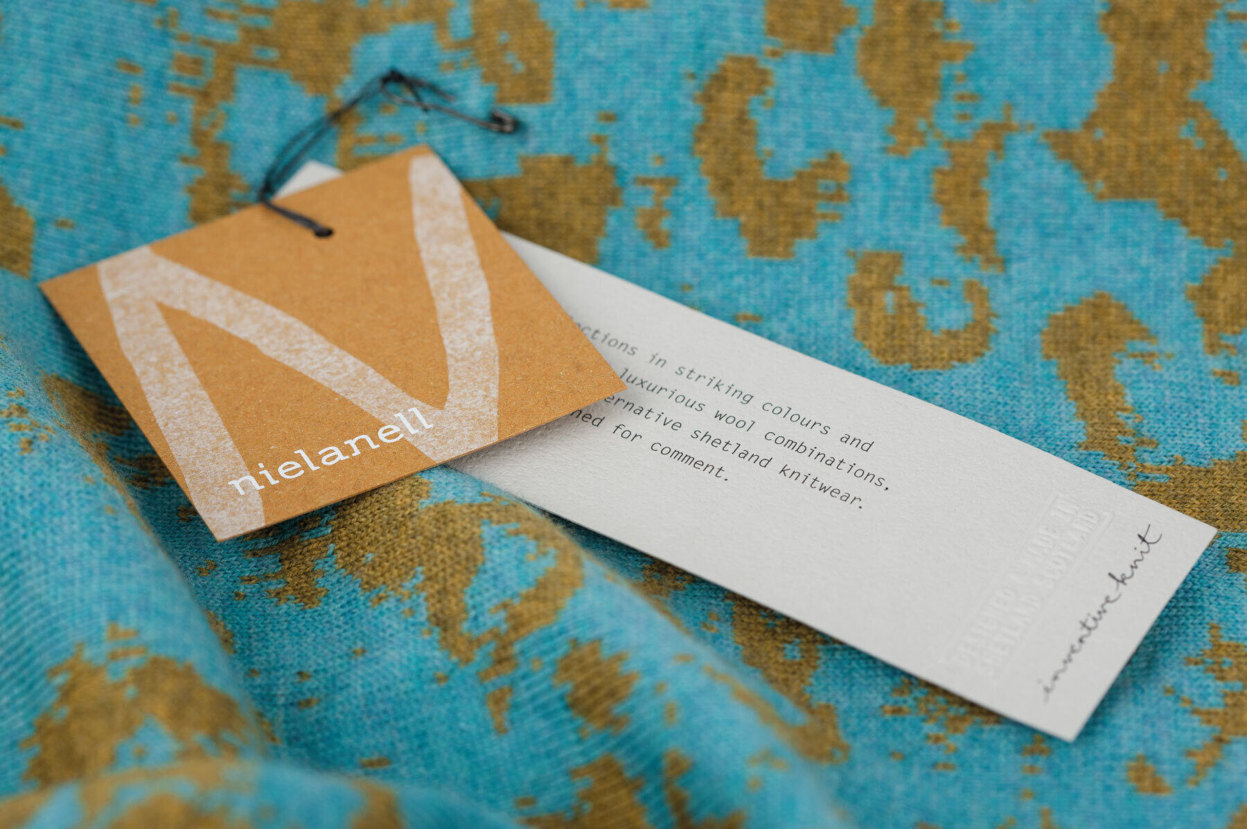 Yellow screenprinted and grey litho printed clothings tags sitting on top of Nielanell knitwear.